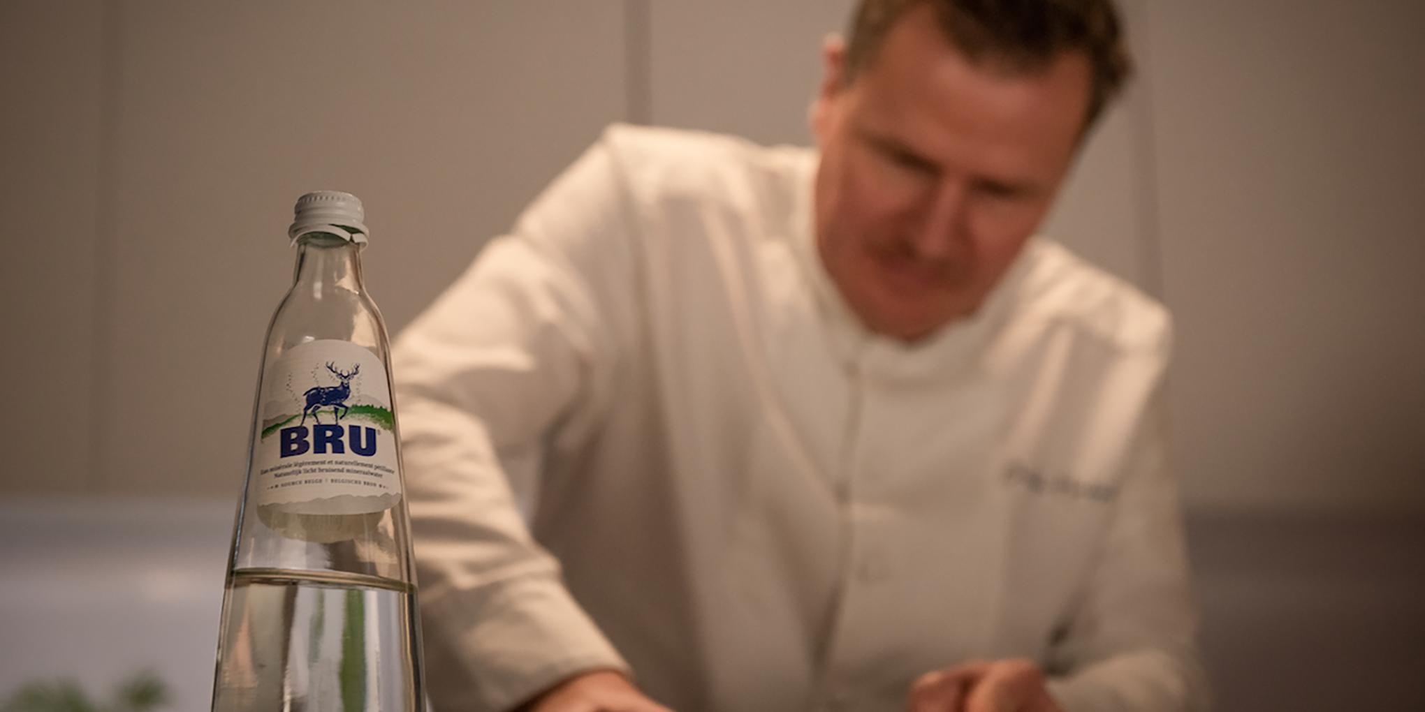 Christophe Hardiquest dans les cuisines de son restaurant Bon-bon avec une bouteille de BRU®