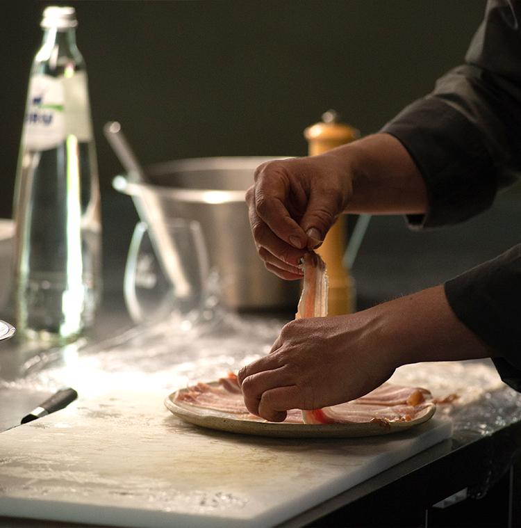 Le chef Stefan Jacobs dans sa cuisine, avec une bouteille de BRU®, prépare des paupiettes de porc pour sa version de la salade liégeoise.
