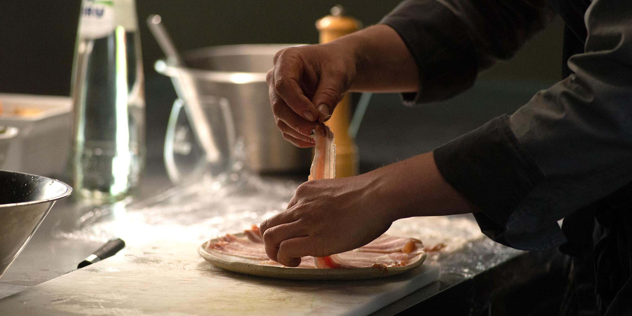 Chef Stefan Jacobs in zijn keuken met fles BRU® maakt varkensrollades voor lokale Luikse Salade
